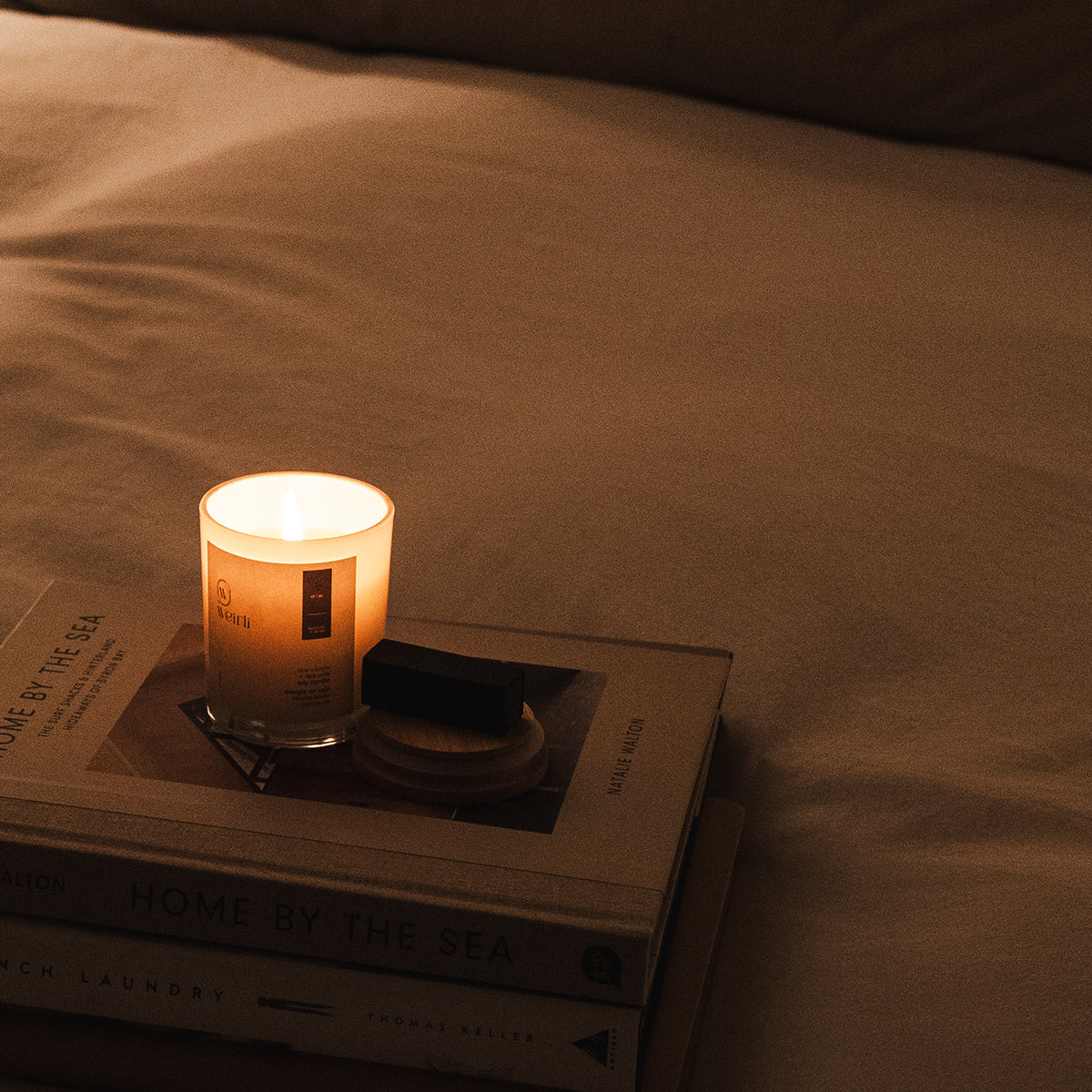 Weirli Raw Vanilla and Rice Milk Soy Candle lit on a bed